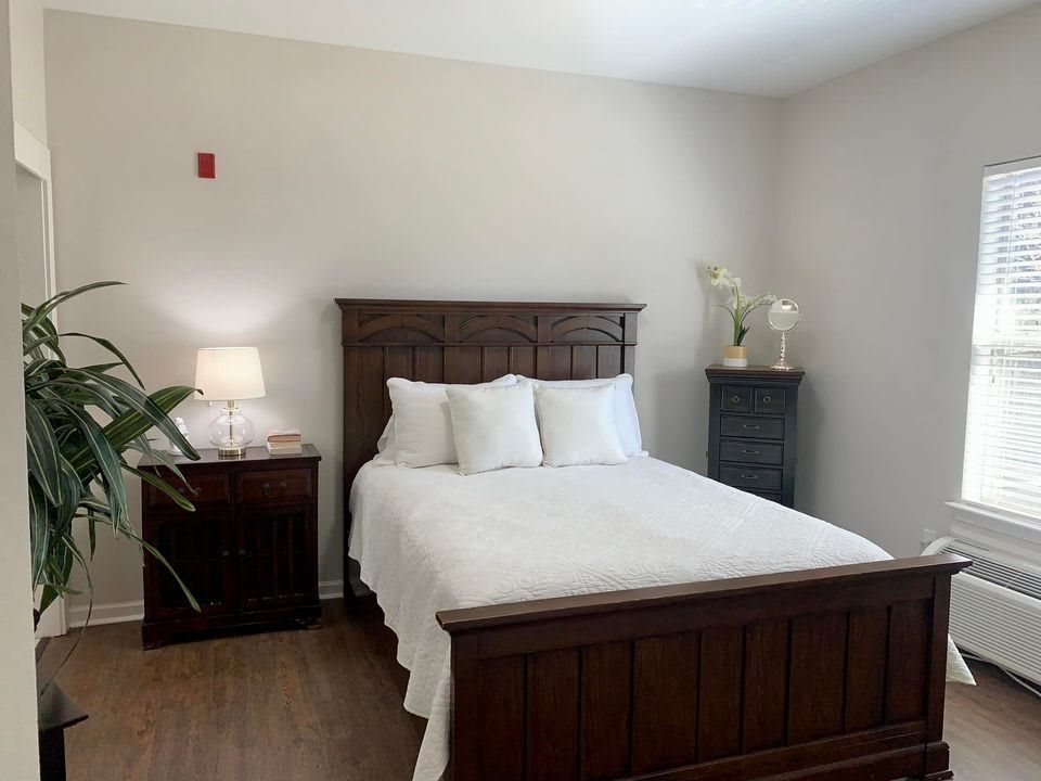 A cozy bedroom featuring a wooden bed frame and white bedding, with matching nightstands and a lamp.