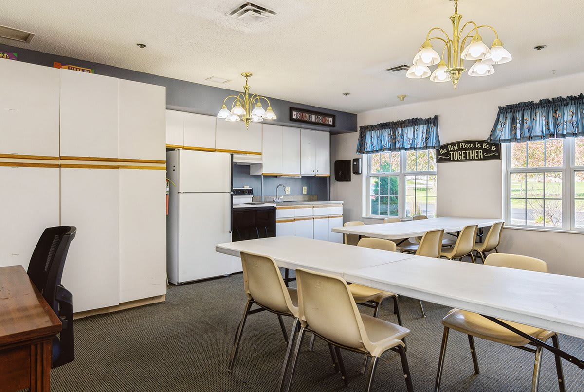 A community kitchen and dining area with multiple tables, chairs, and bright lighting.