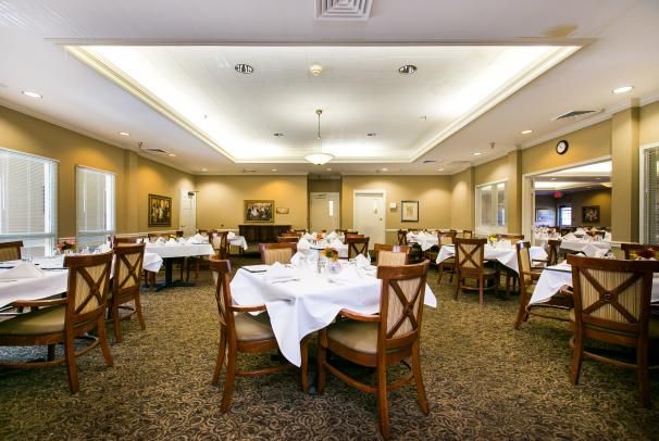 An elegant dining room with neatly arranged tables and chairs, featuring white tablecloths and soft lighting.