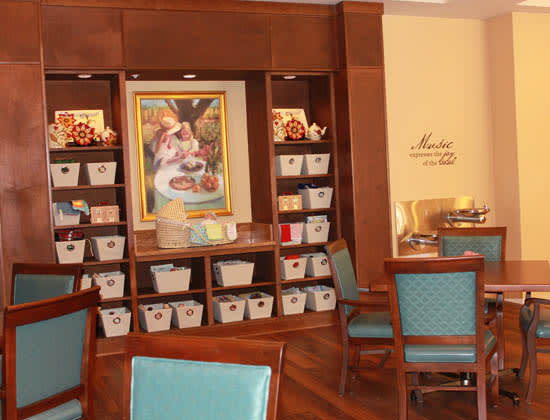 A cozy room with shelves filled with baskets, framed artwork on the wall, and comfortable chairs arranged around the space.