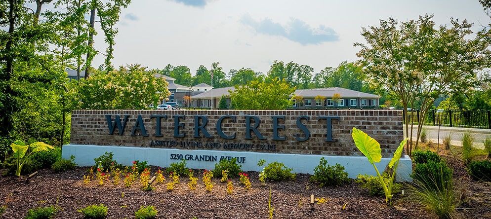 An entrance sign for 'Watercrest' with surrounding greenery and buildings in the background.