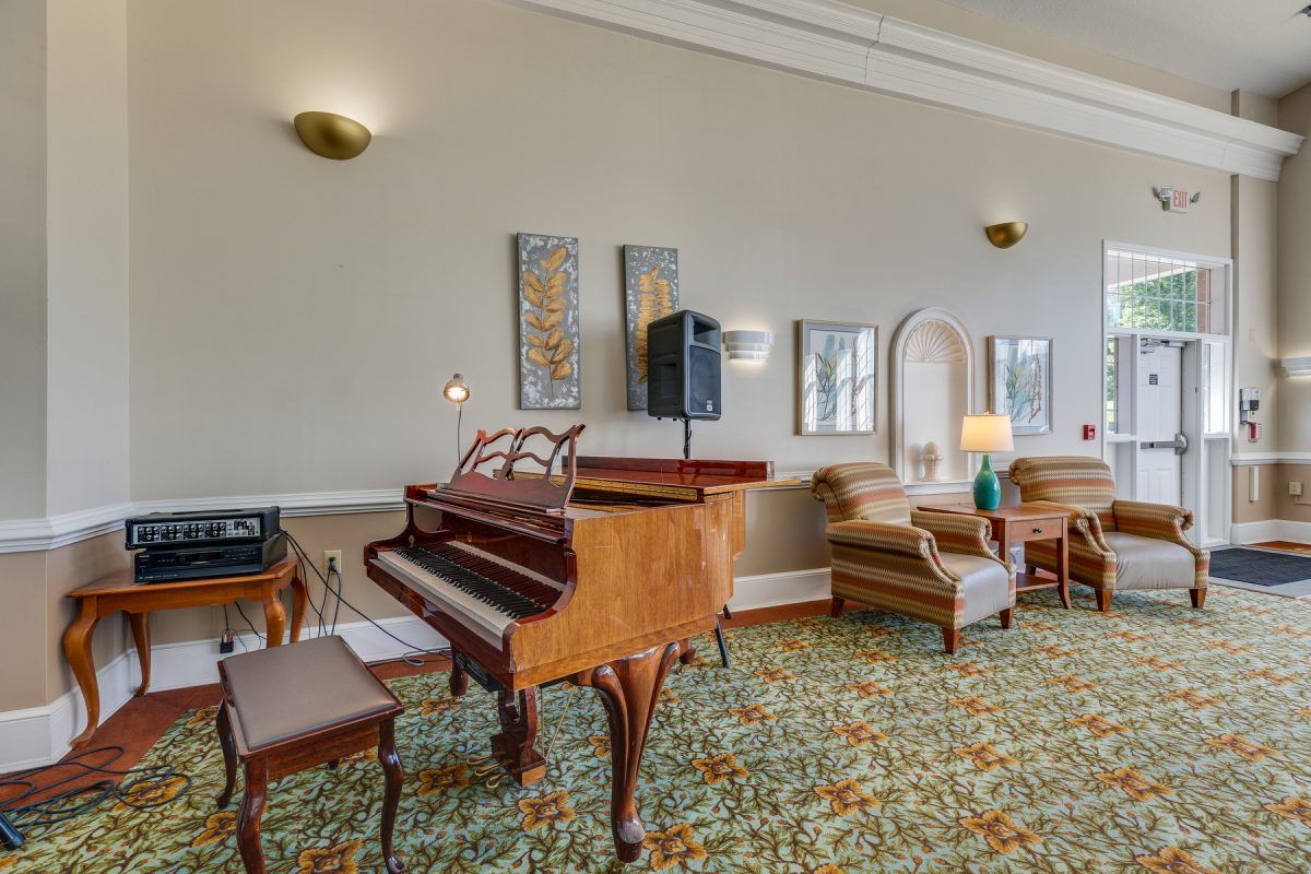 A cozy living room featuring a grand piano, upholstered armchairs, and elegant decor.