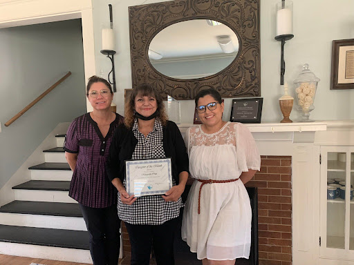 A joyful moment of recognition as three women gather together to celebrate an achievement.
