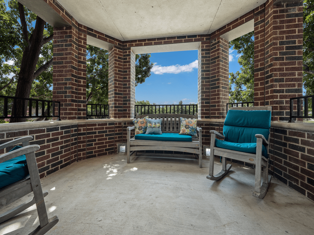 A cozy porch with comfortable seating and a scenic view through brick-framed windows.