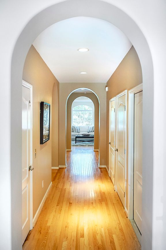 A bright hallway with wooden floors and arched doorways leading to a well-lit room.