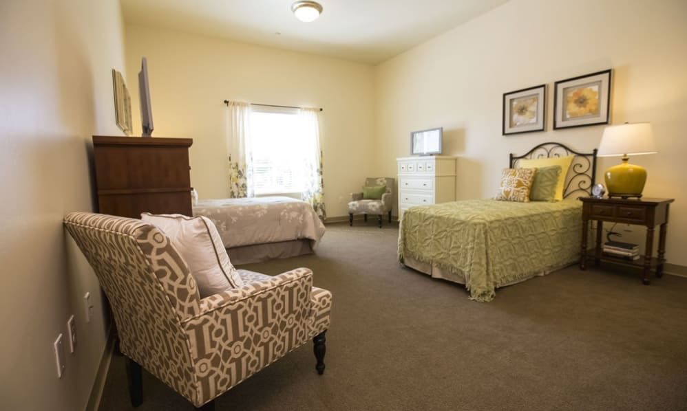 A cozy bedroom featuring a single bed, an armchair, and a dresser near a window.