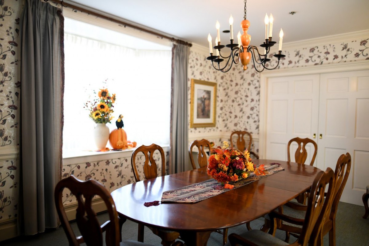 A cozy dining room with elegant decor, featuring a wooden table set for autumn with pumpkins and flowers.