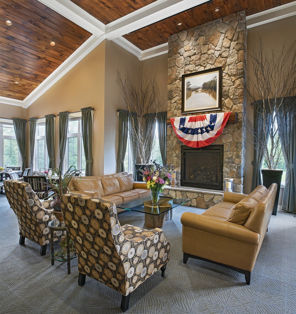 A spacious living room featuring a stone fireplace, elegant sofa set, and large windows with decorative curtains.