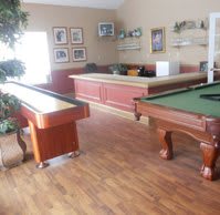 A cozy game room with a billiard table and shuffleboard setup, featuring hardwood flooring and casual seating.