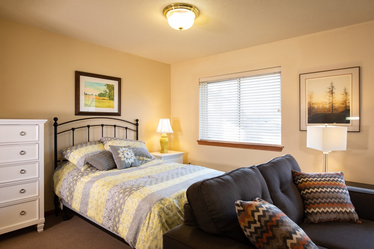 A cozy bedroom with a bed, sofa, and warm lighting.