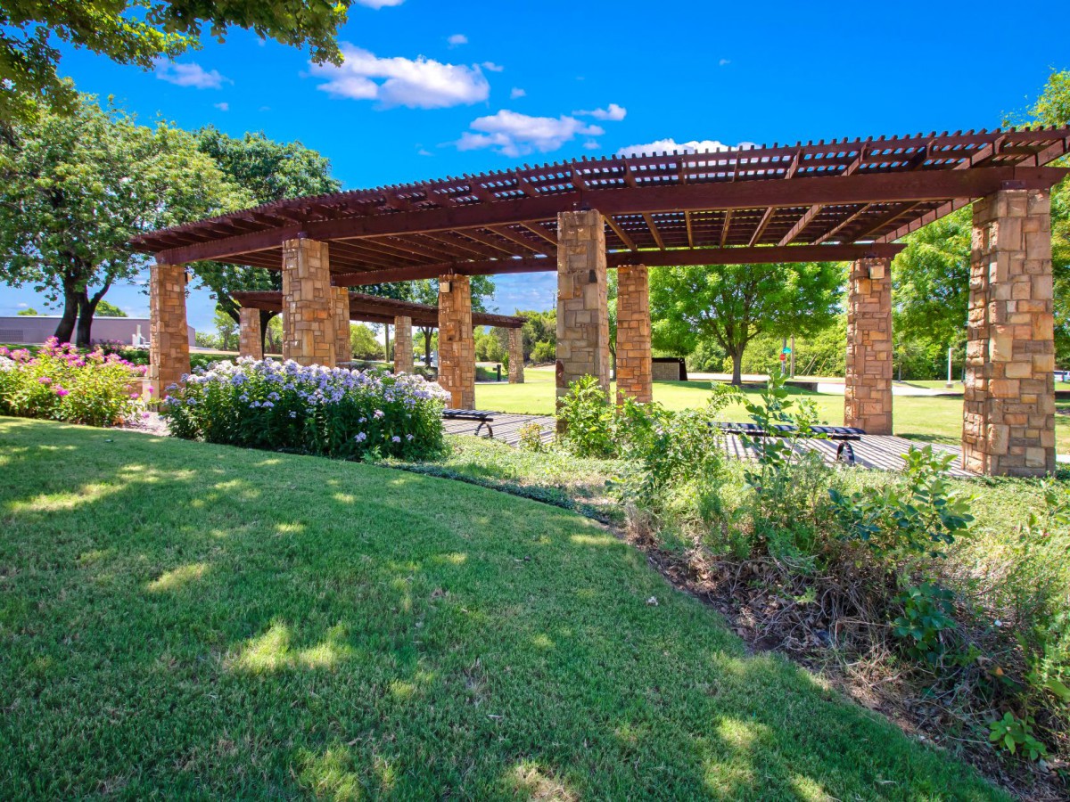 A beautiful park with a pergola surrounded by lush greenery on a sunny day.