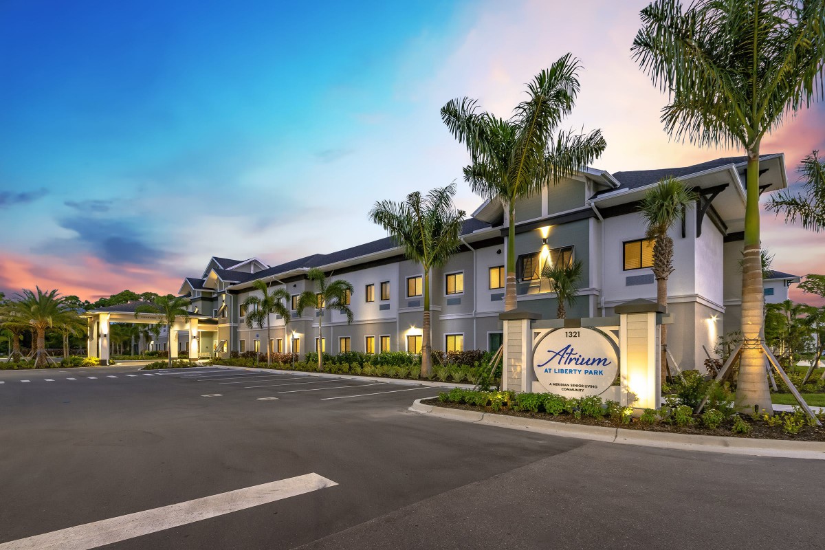 A modern hotel building with palm trees, photographed in the evening.