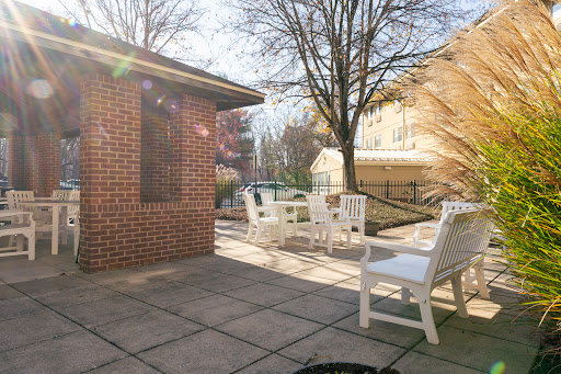 A sunny patio area featuring white outdoor furniture surrounded by trees.