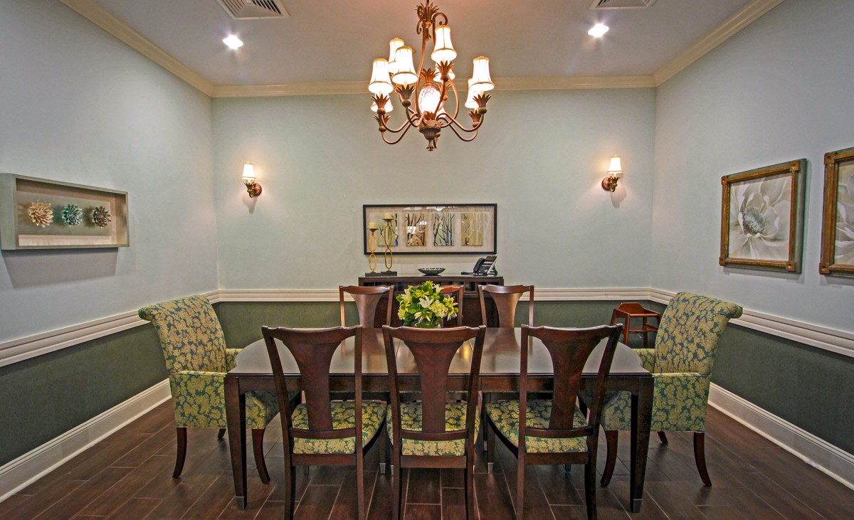 A classic dining room featuring a wooden table set with patterned chairs, illuminated by a chandelier and wall sconces.