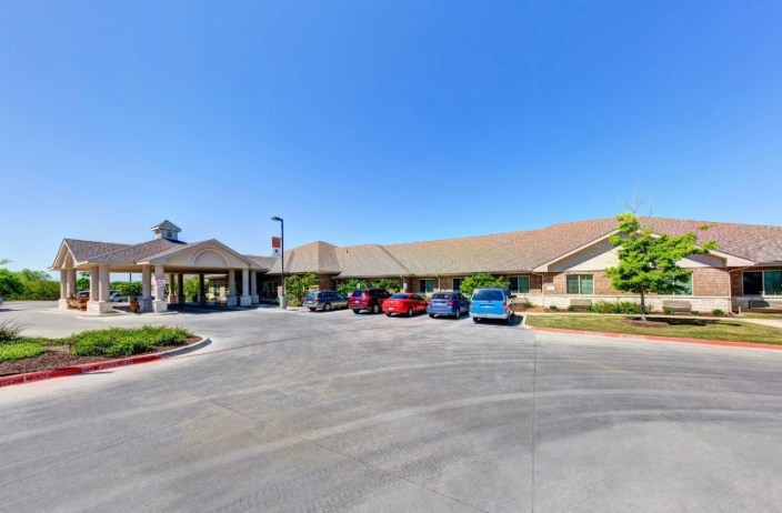 A wide view of a building with a parking lot and several cars under a clear blue sky.