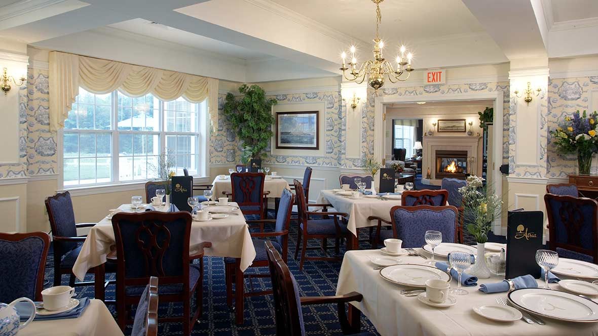 An elegant dining room with neatly arranged tables and chairs, illuminated by a chandelier.