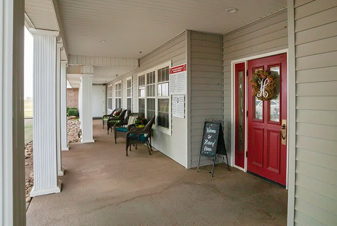 A cozy porch with chairs and a red door adorned with a wreath.