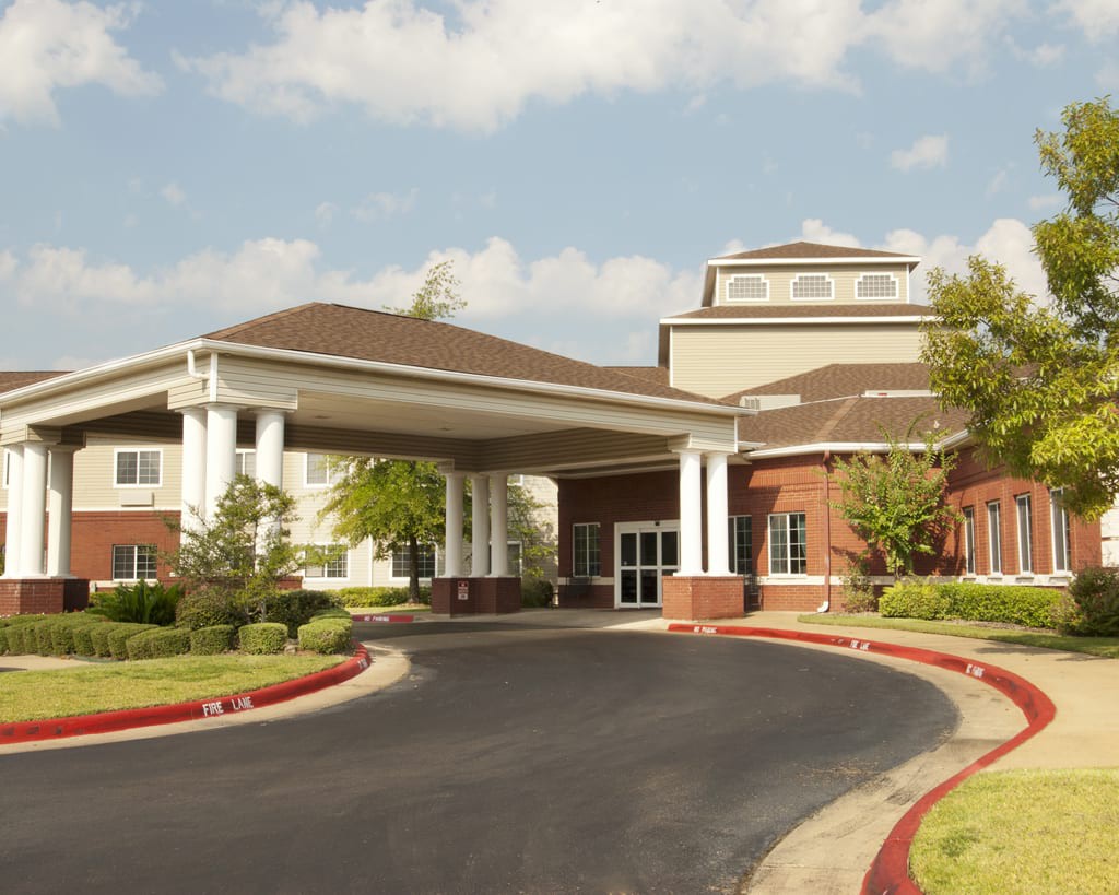 A large building with a covered entrance and circular driveway under a partly cloudy sky.