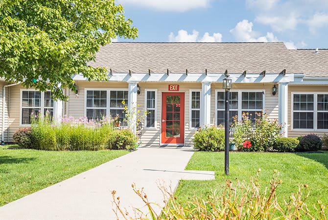 A charming house with a red door, surrounded by a well-maintained garden on a sunny day.