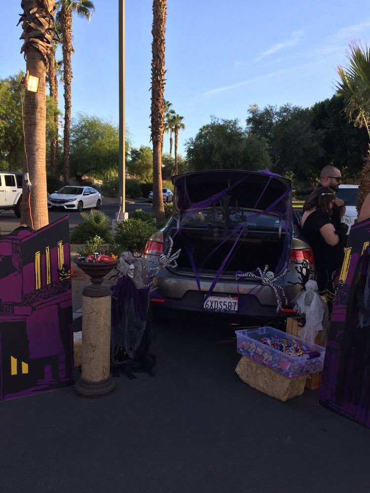 A car trunk decorated in a purple theme for a trunk or treat event, surrounded by Halloween decorations and participants.