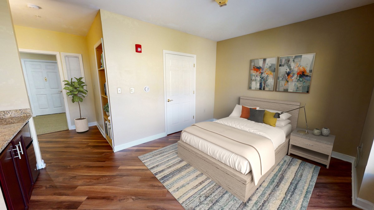 A cozy bedroom featuring a neatly made bed with decorative pillows, a large abstract painting above the headboard, and a striped rug on wooden flooring.