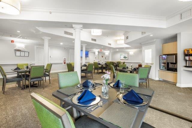 A modern dining room with neatly arranged tables and chairs, featuring blue napkins and floral centerpieces.