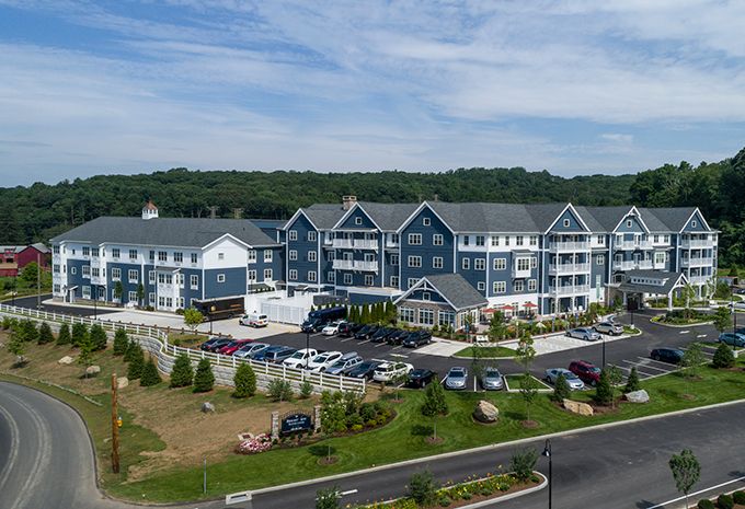 Aerial view of a modern residential building complex with a parking lot and landscaped surroundings.