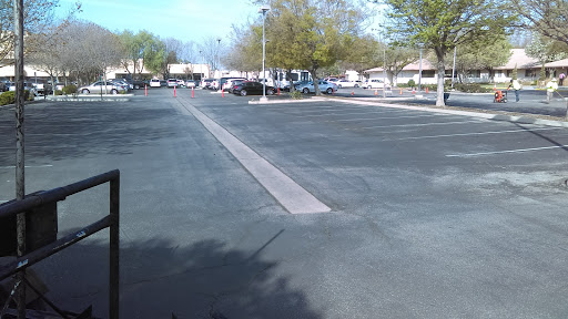 A spacious, empty parking lot during the day, lined with trees and a few parked vehicles.