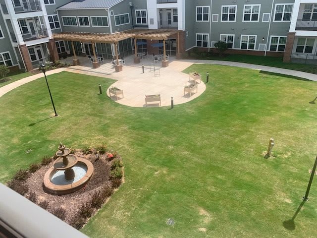 A well-maintained courtyard featuring a central fountain, surrounded by grass and benches, adjacent to a multi-story building.