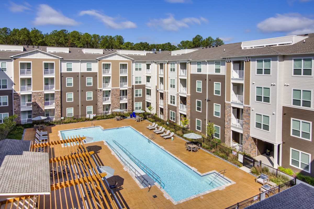 A modern apartment complex featuring a central swimming pool and outdoor seating area.
