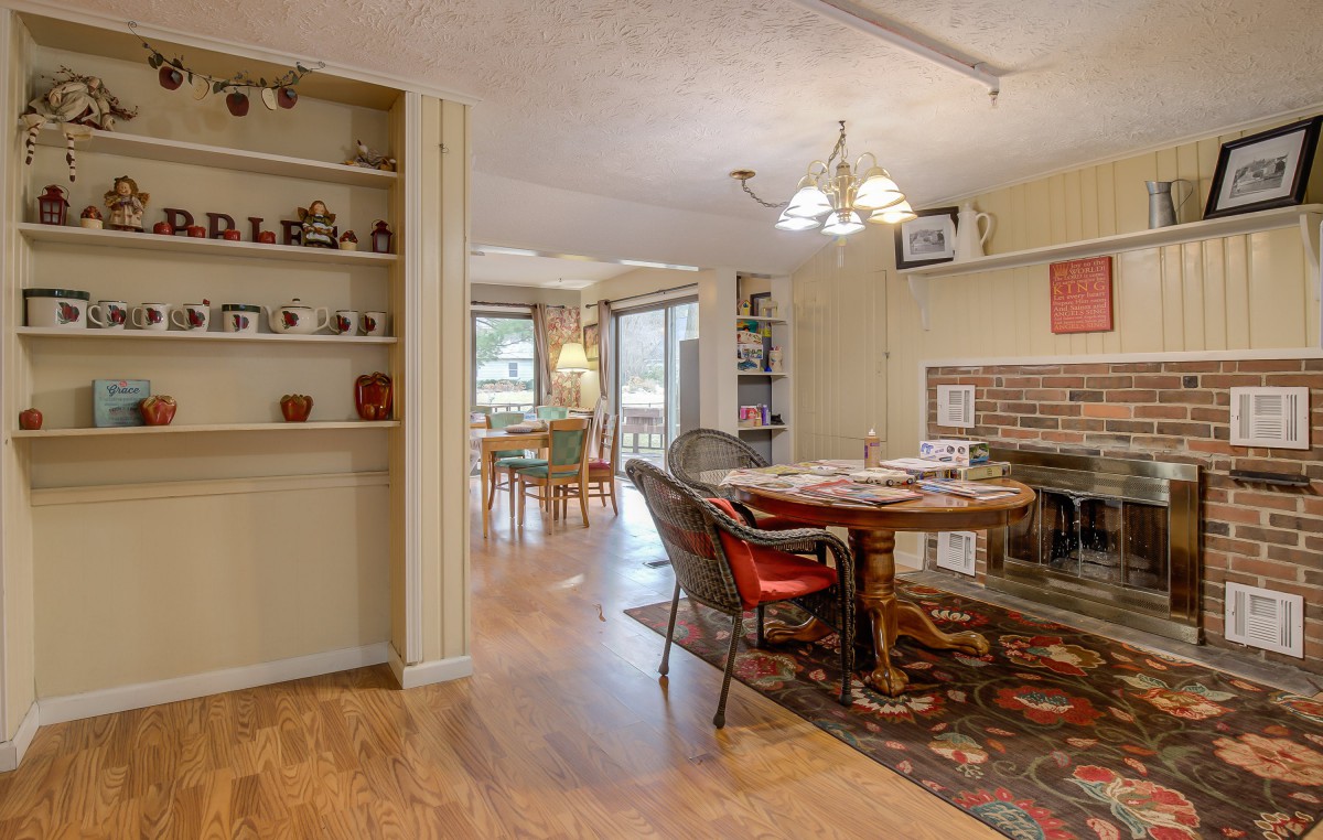 A cozy dining room with an open floor plan featuring a brick fireplace and elegant chandelier.