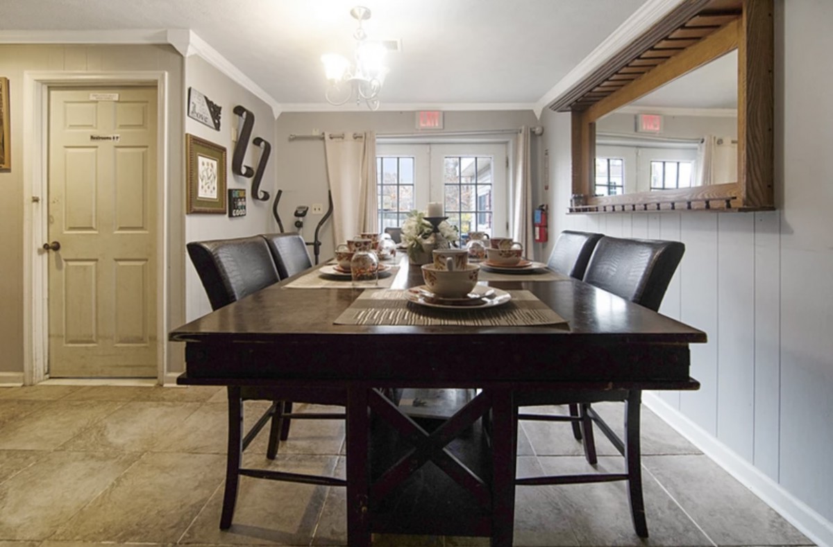 A stylish dining room featuring a dark wooden table set with plates and decor, surrounded by elegant chairs and illuminated by overhead lighting.