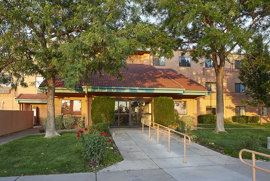 A building entrance with a pathway lined by trees and shrubs.