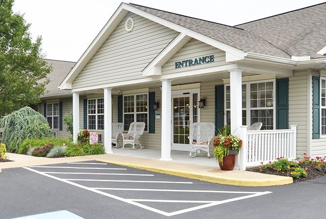 A suburban building entrance with a porch, chairs, and potted plants.