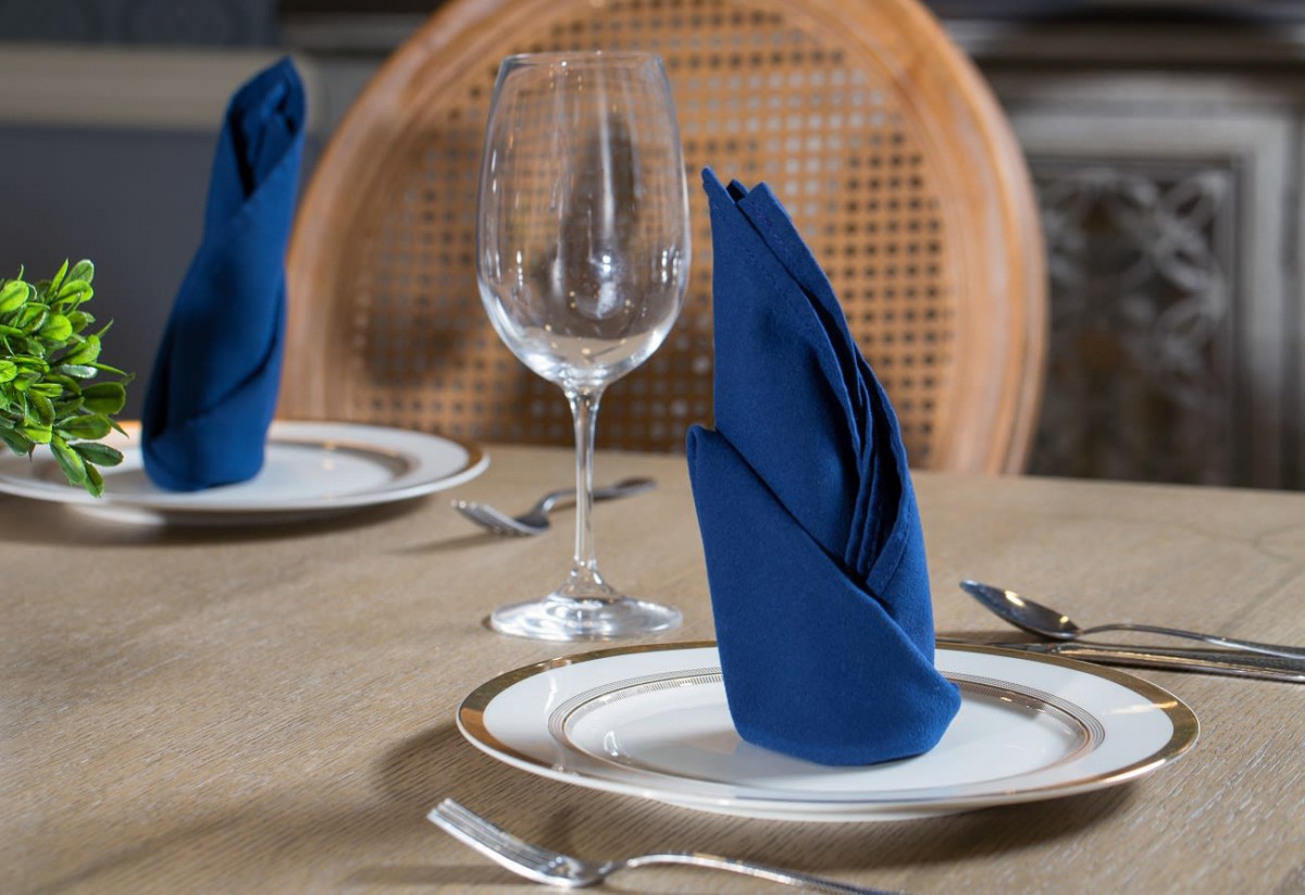 Elegant dining table setup with a blue folded napkin and wine glass.