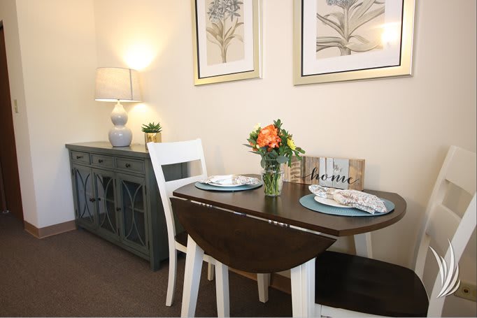A cozy dining area with a small table set for two, adorned with a flower arrangement and surrounded by elegant decor.