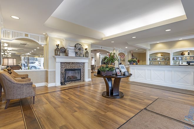 A spacious, elegantly decorated lobby with a wooden floor, fireplace, and central table with plants.