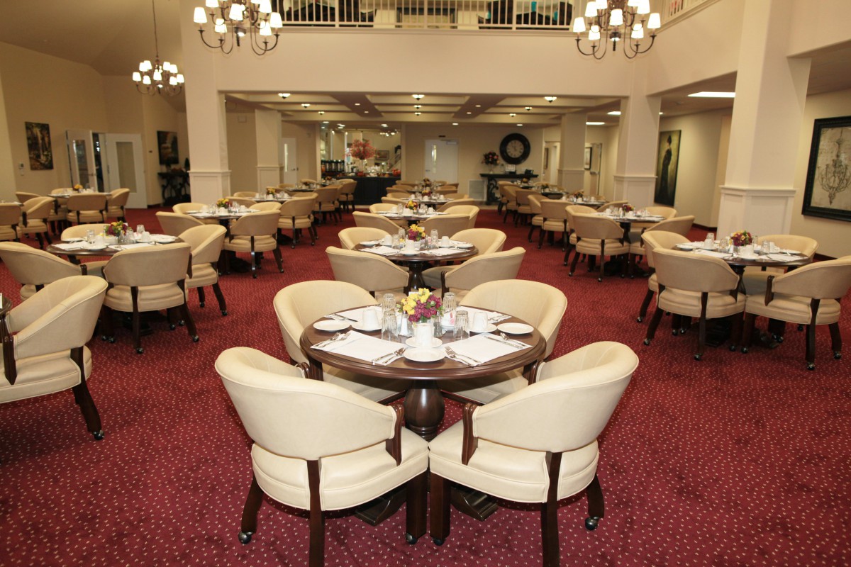 Elegant dining room with neatly arranged tables and chairs, featuring a red carpet and chandeliers.