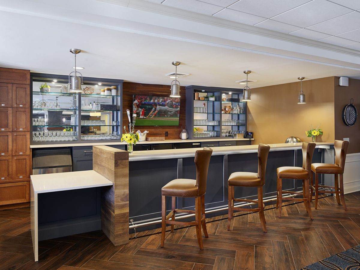 A modern bar area with a sleek counter and high stools, featuring stylish lighting and decor.