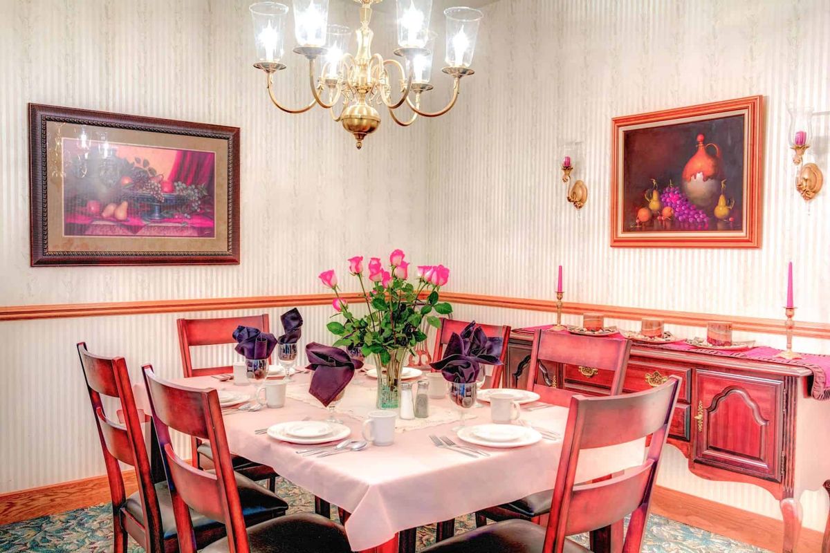 A well-decorated dining room with a table set for a meal, featuring flowers and a chandelier.