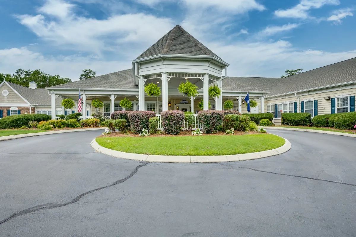 A building with a circular driveway and well-maintained landscaping under a partly cloudy sky.