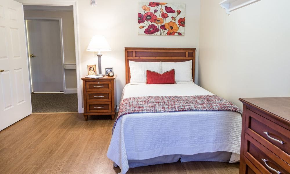 A cozy bedroom with a neatly made bed, wooden nightstand, and decorative painting.
