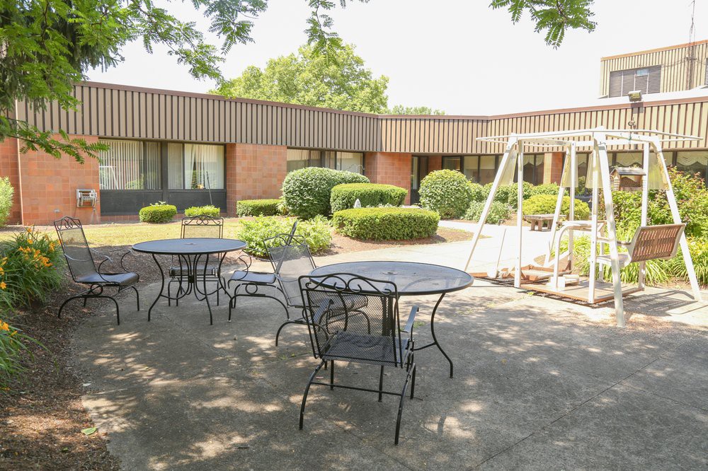 A peaceful courtyard with patio tables, chairs, and a swing surrounded by greenery.