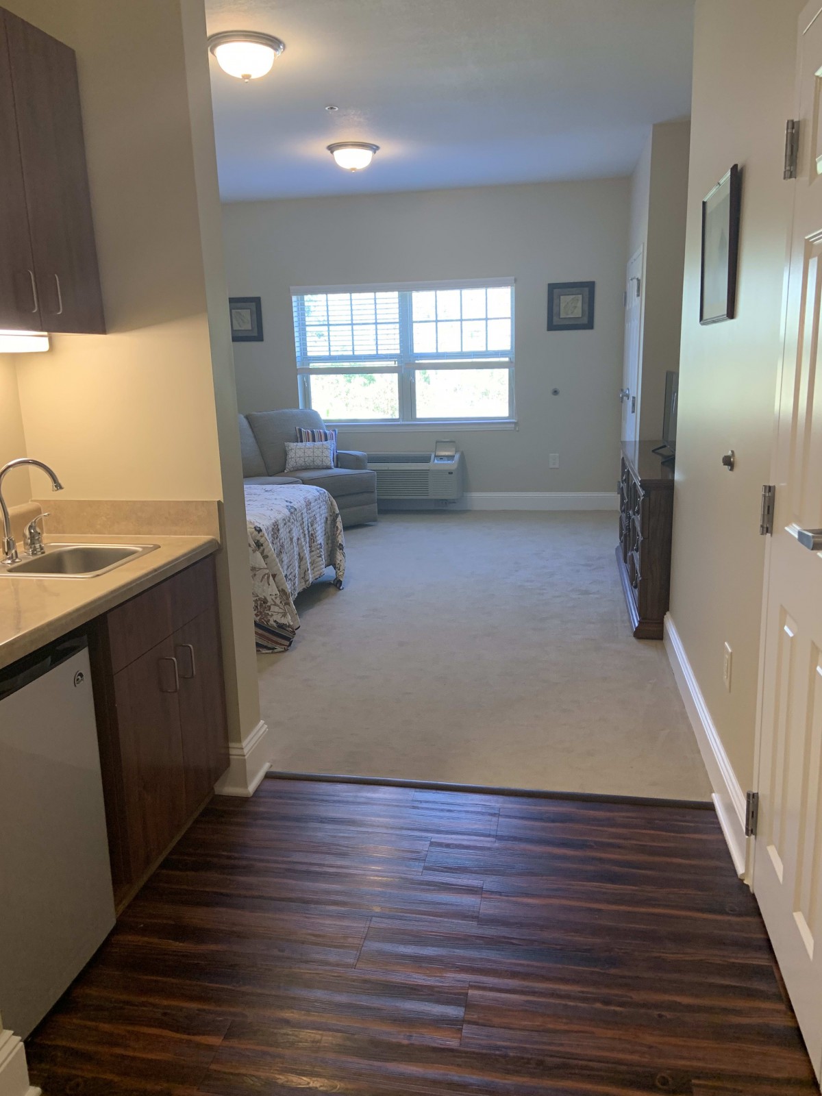 A cozy room featuring a bedroom area with carpeting and an adjoining kitchenette with wood flooring.