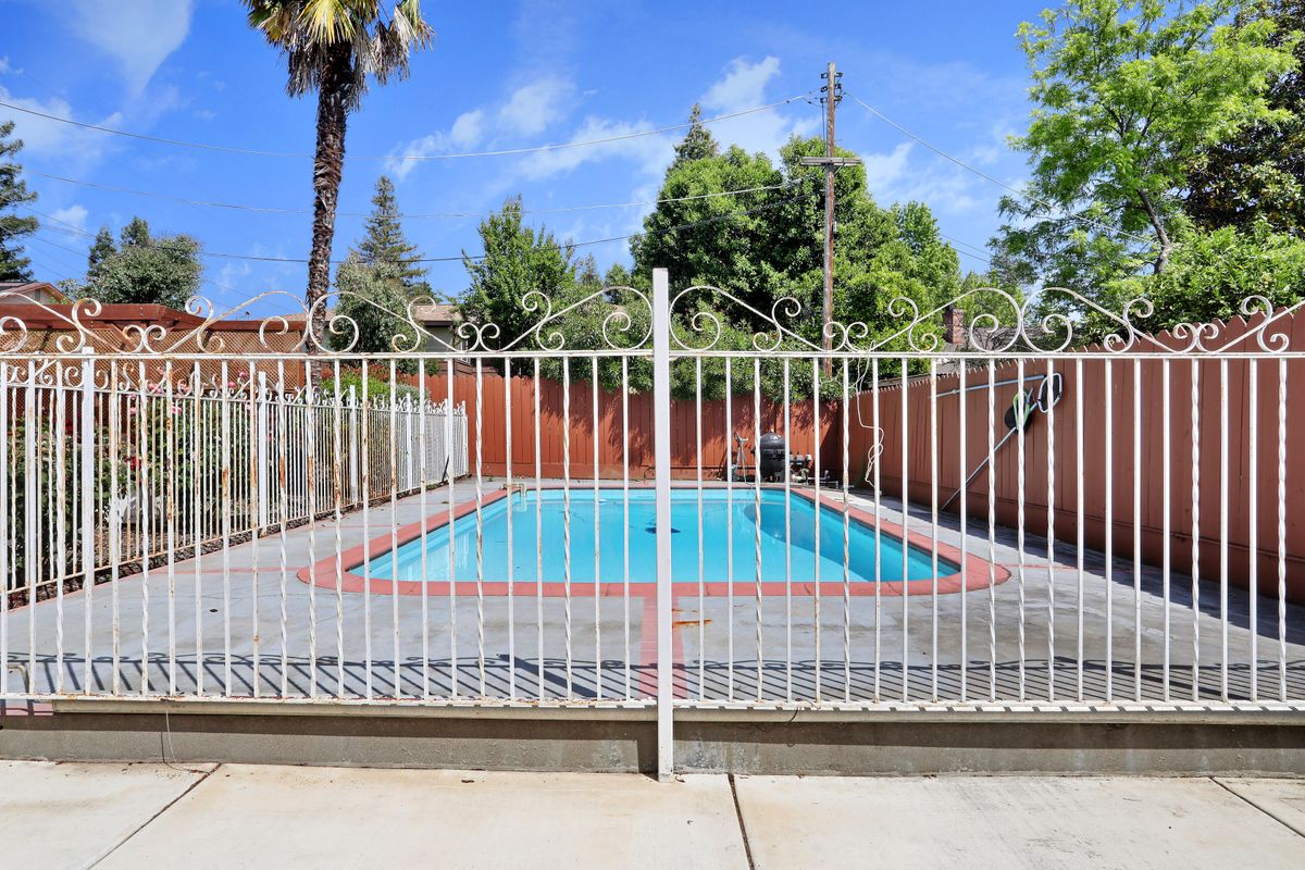An outdoor swimming pool surrounded by a fence with trees and a clear blue sky in the background.