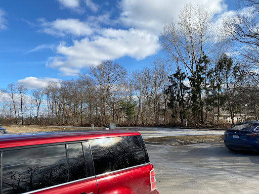 A red car parked outdoors under a partly cloudy sky with trees in the background.