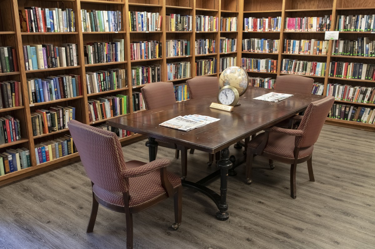 A cozy library reading room with a wooden table surrounded by chairs and bookshelves.