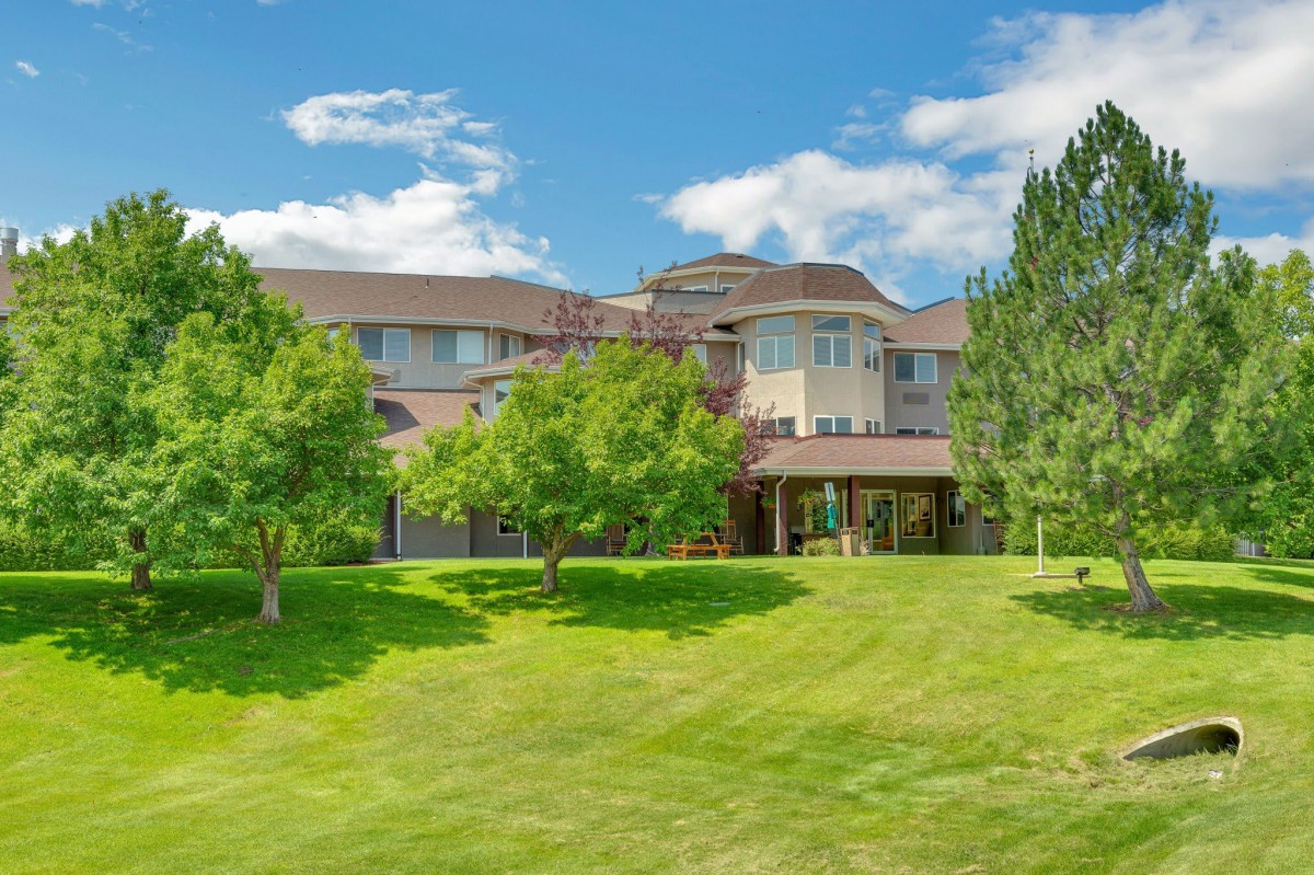 A beautiful house surrounded by a lush green lawn and trees under a clear blue sky.