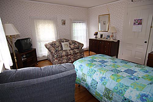 A cozy bedroom with vintage decor featuring a bed, armchair, and dresser.