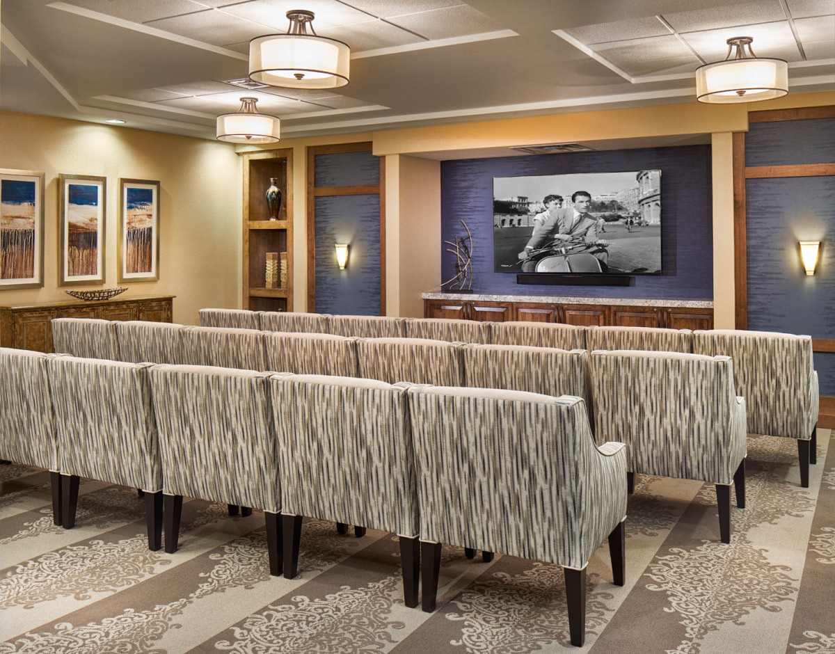 A well-designed theater room with rows of patterned chairs facing a large screen, featuring elegant ceiling lights.